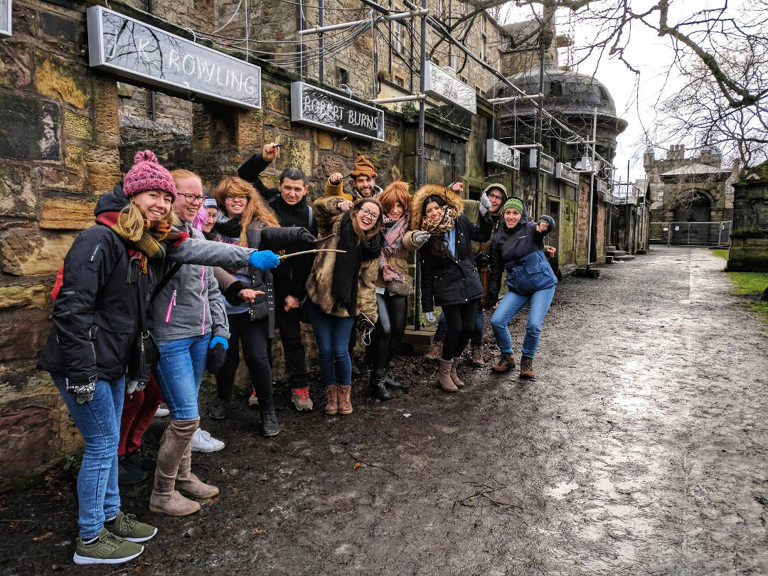 A Harry Potter tour in Greyfriars Kirkyard poses beneath JK Rowling's name in neon light